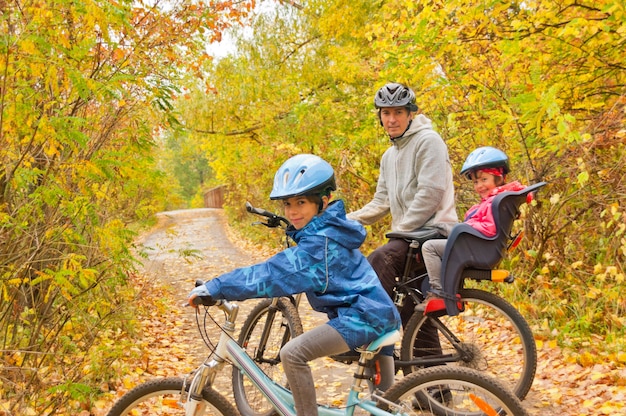 Family cycling outdoors, golden autumn in park. Father and kids on bikes. Family sport