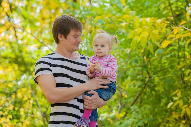 Papà di famiglia e figlia per una passeggiata nel parco in autunno. il bambino è nelle mani sicure del padre