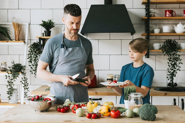 family dad young man and son teenage boy cook vegetable salad in kitchen and spend quality time together father and son talking and cooking vegetarian food and doing chores 8 march and mothers day