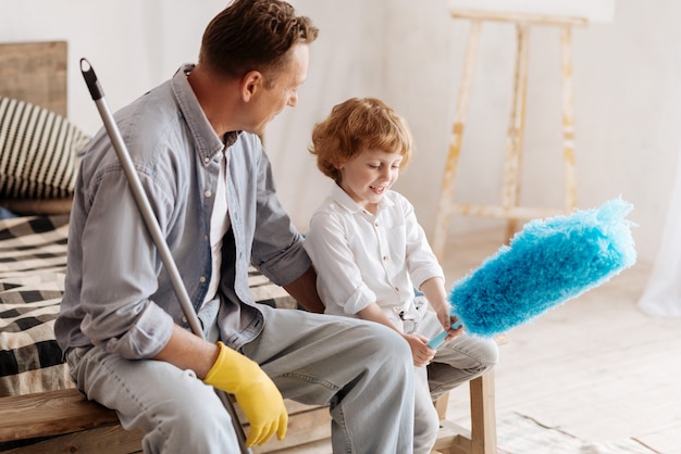 Family day. Happy male person sitting near son and turning head while looking forward, going to do cleaning