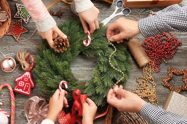 Family decorating christmas wreath  on wooden surface