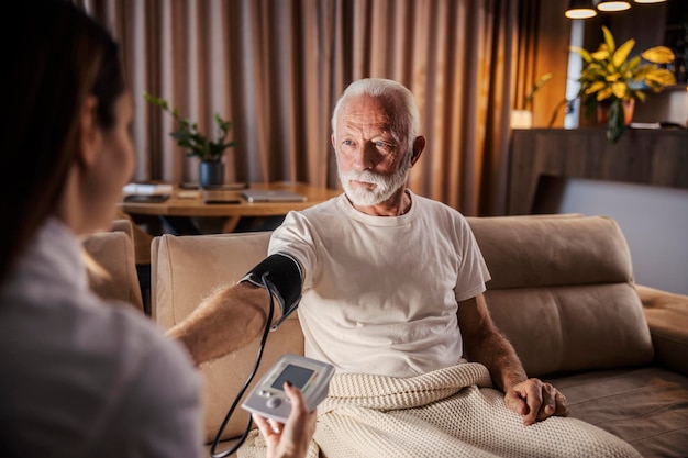 a family doctor is measuring blood pressure on her senior patient during home visit