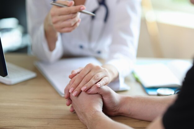 Family doctor supports patient after revealing severe diagnosis sitting at table in clinic