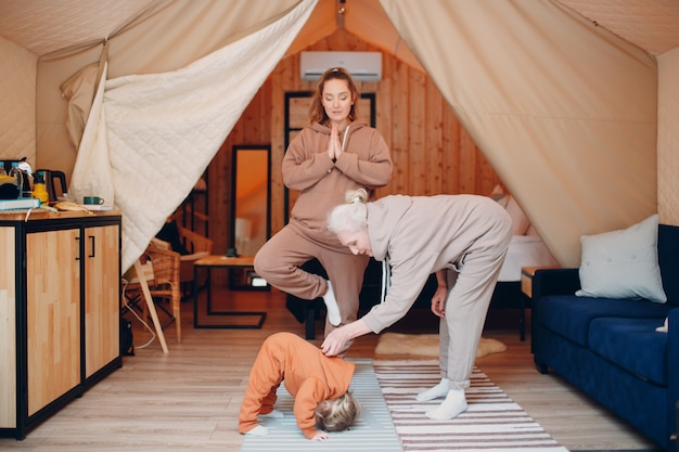 Family doing exercises sports idoors. Young and senior elderly woman relaxing at glamping camping tent. Mother and daughter modern at fitness vacation lifestyle concept.