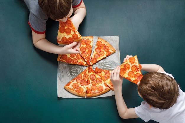 Family eating peperoni pizza. Kids holding a slice of pizza.