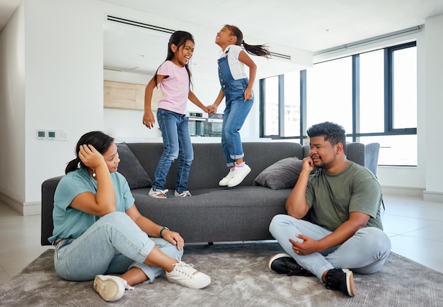 Family energy and kids jumping on home sofa with tired parents struggling with naughty hyperactive and playing children Woman and man with ADHD noisy and laughing girls friends or fun twins