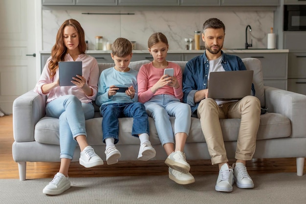 Photo family engaged with technology sitting on couch