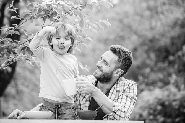 Family enjoy homemade meal Father son eat food and have fun Food habits Little boy with dad eating food nature background Summer breakfast Healthy food concept Feeding baby Menu for children