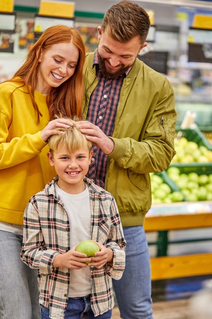 Foto la famiglia si diverte a fare shopping con il bambino, i giovani genitori nel corridoio del supermercato con il ragazzo carino, in abbigliamento casual, si divertono