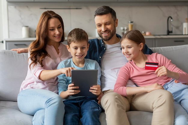 Foto famiglia che si godono insieme il tablet a casa usando una carta di credito