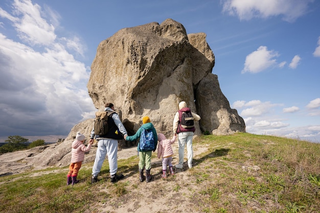 自然を探索する家族両親を持つ子供たちは、ウクライナのピドカミンの丘で大きな石にハイキングするバックパックを着用します