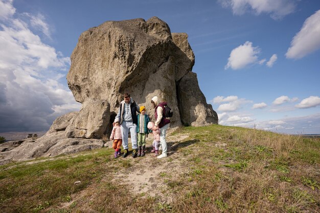 Family exploring nature Children with parents wear backpack hiking against big stone in hill Pidkamin Ukraine