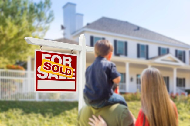 Photo family facing sold for sale real estate sign and house