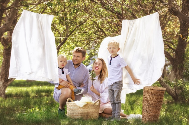 家族の父母と美しくて幸せな2人の息子が一緒に庭にきれいな洗濯物を掛けます