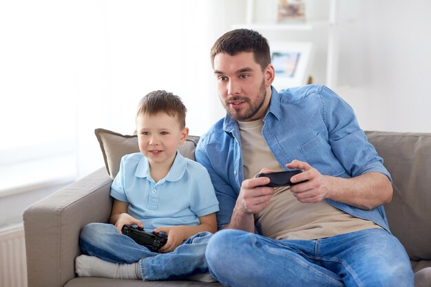 家族,父親,人々のコンセプト - 幸せな父親と小さな息子がゲームパッドで家でビデオゲームをしています