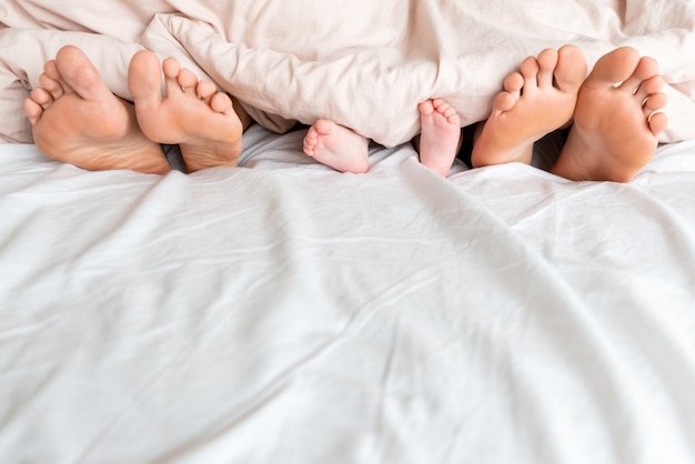 Family feet under the white blanket in the bed