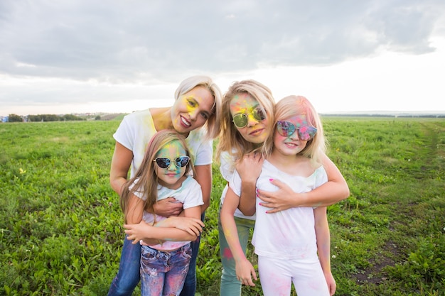 Famiglia, festival di holi e concetto di vacanze - close up ritratto di madri e figlie ricoperte di vernice.