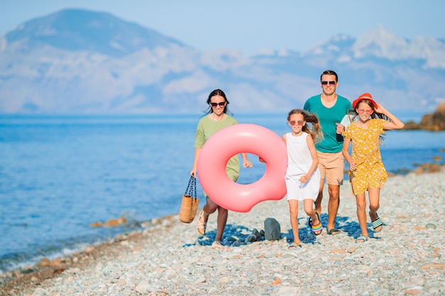 Famiglia di quattro persone sulla spiaggia divertendosi. bambini e genitori corrono in riva al mare