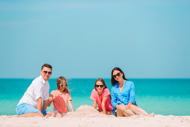 Famiglia di quattro che fa il castello della sabbia alla spiaggia bianca tropicale