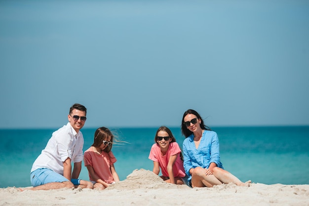 Family of four making sand castle at tropical white beach