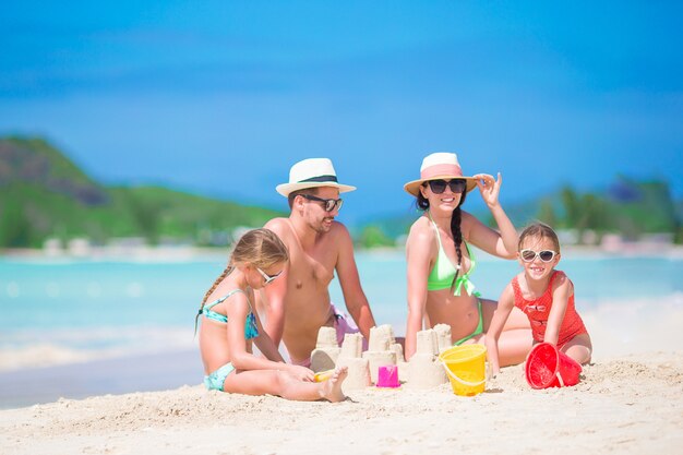 Family of four making sand castle at tropical white beach