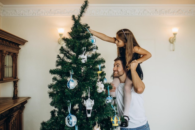 Family of four parents pregnant mom and dad and two siblings little boy and girl in stylish clothes in chalet are ready to welcome Christmas and New Year near Christmas tree with gift box presents