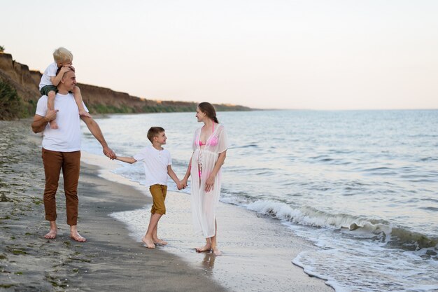 family of four walking along the seashore. parents and two sons. happy friendly family
