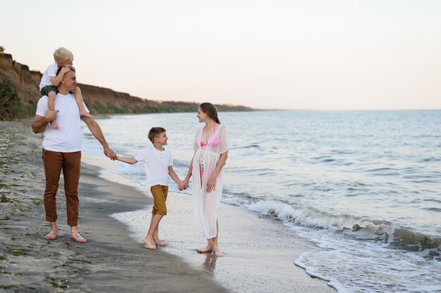 Famiglia di quattro persone che cammina lungo la riva del mare. genitori e due figli. felice famiglia amichevole