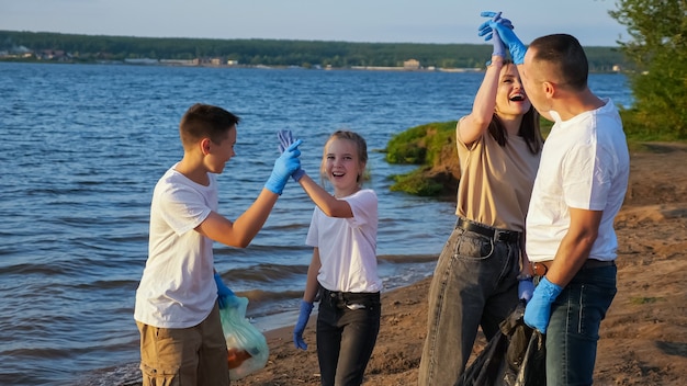 10代の若者がプラスチックの破片からビーチを片付けている4人家族。環境教育のコンセプト。