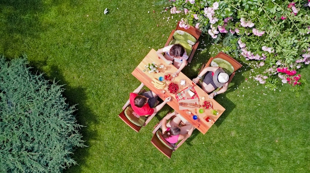 Family and friends eating together outdoors on summer garden party. Aerial view of table with food and drinks from above. Leisure, holidays and picnic concept