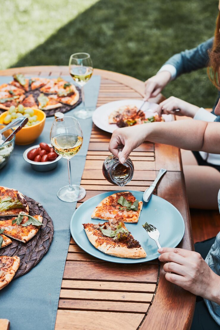 Photo family and friends having meal - pizza salads fruits and drinking white wine during summer picnic