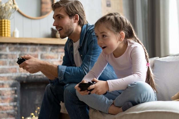 家族のゲームとエンターテイメントのコンセプト自宅でビデオ ゲームをプレイするゲームパッドを持つ幸せな父と小さな娘