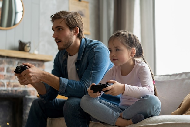 Family, gaming and entertainment concept - happy father and\
little daughter with gamepads playing video game at home.