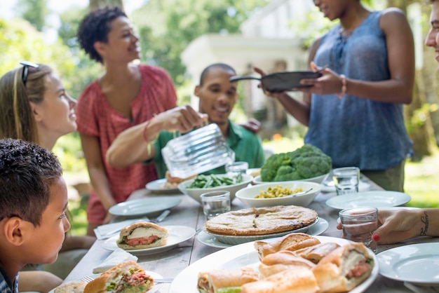 A family gathering men women and children around a table in a\
garden in summer