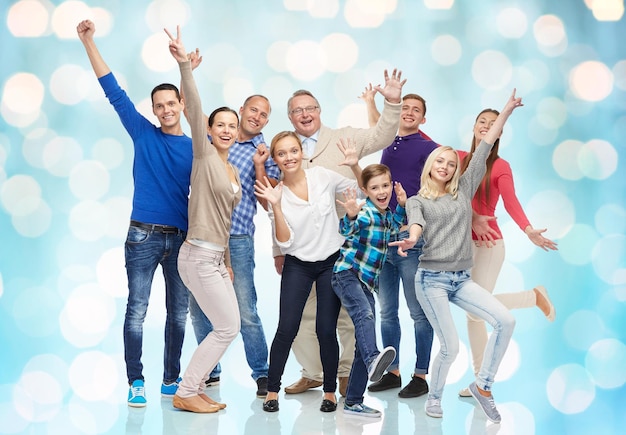 family, gender, generation and people concept - group of smiling men, women and boy having fun and waving hands over blue holidays lights background