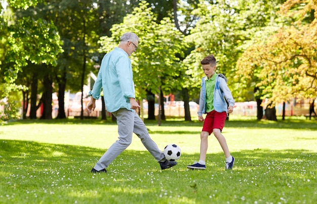 family, generation, game, sport and people concept - happy grandfather and grandson playing football at summer park