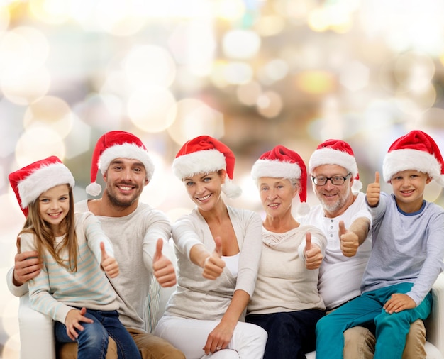 family, generation, gesture, holidays and people concept - happy family in santa helper hats showing thumbs up over lights background