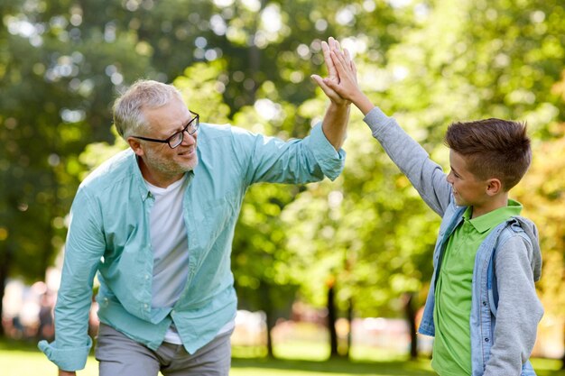 가족, 세대, 제스처 및 사람 개념 - 행복한 할아버지와 손자가 여름 공원에서 하이파이브를 합니다.