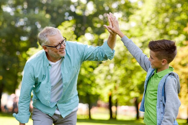 family, generation, gesture and people concept - happy grandfather and grandson making high five at summer park