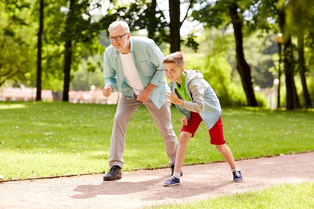 family, generation and people concept - happy grandfather and grandson racing at summer park