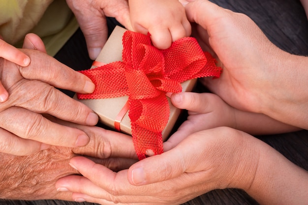 Family hands hold the gift box. several generations of family keep the gift with the red bow