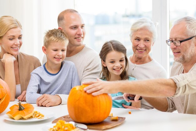 family, happiness, generation, holidays and people concept - happy family making halloween pumpkins at home