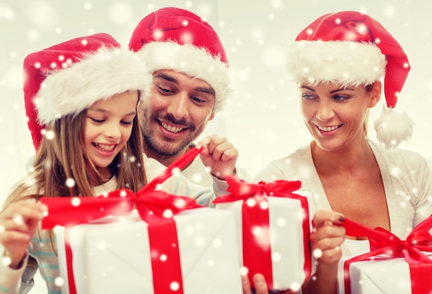 family, happiness, generation, holidays and people concept - happy family in santa helper hats with gift boxes sitting on couch at home