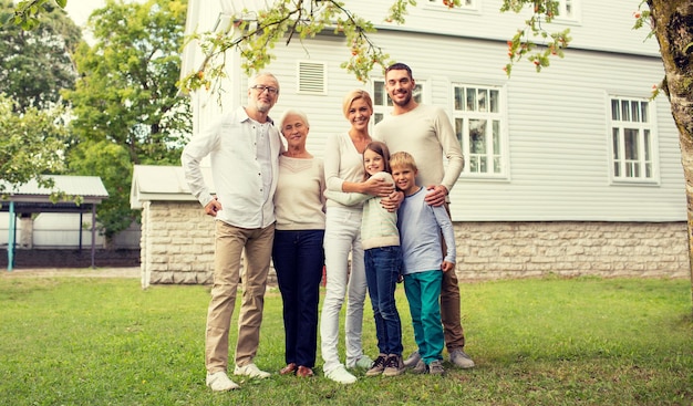 Concetto di famiglia, felicità, generazione, casa e persone - famiglia felice in piedi davanti alla casa all'aperto