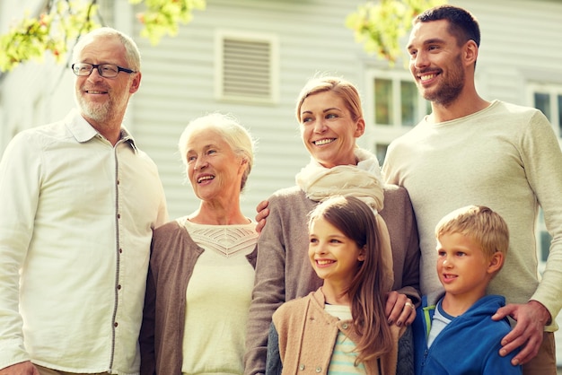 family, happiness, generation, home and people concept - happy family standing in front of house outdoors