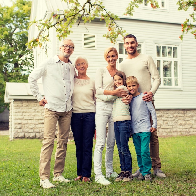 family, happiness, generation, home and people concept - happy family standing in front of house outdoors