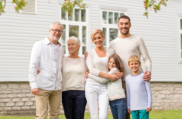 Concetto di famiglia, felicità, generazione, casa e persone - famiglia felice in piedi davanti alla casa all'aperto