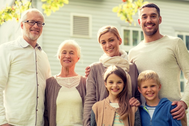 family, happiness, generation, home and people concept - happy family standing in front of house outdoors