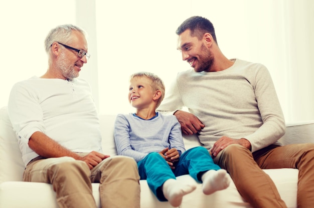 концепция семьи, счастья, поколения и людей - улыбающиеся отец, сын и дедушка сидят дома на диване