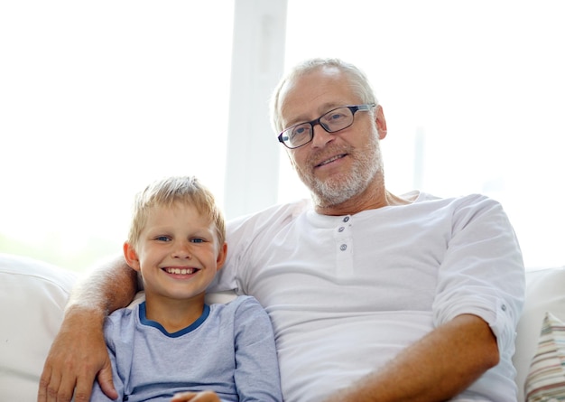 family, happiness, generation and people concept - smiling grandfather with grandson sitting on couch at home